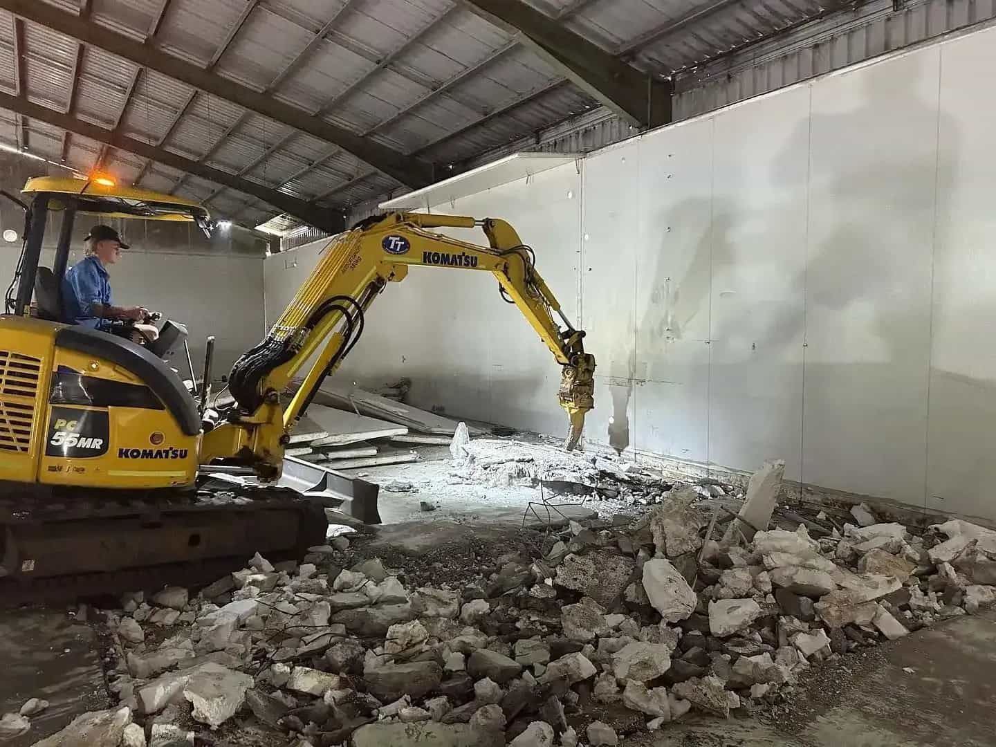 A Man Is Driving A Yellow Excavator In A Warehouse — Tymmo's Tippers In Ballina, NSW