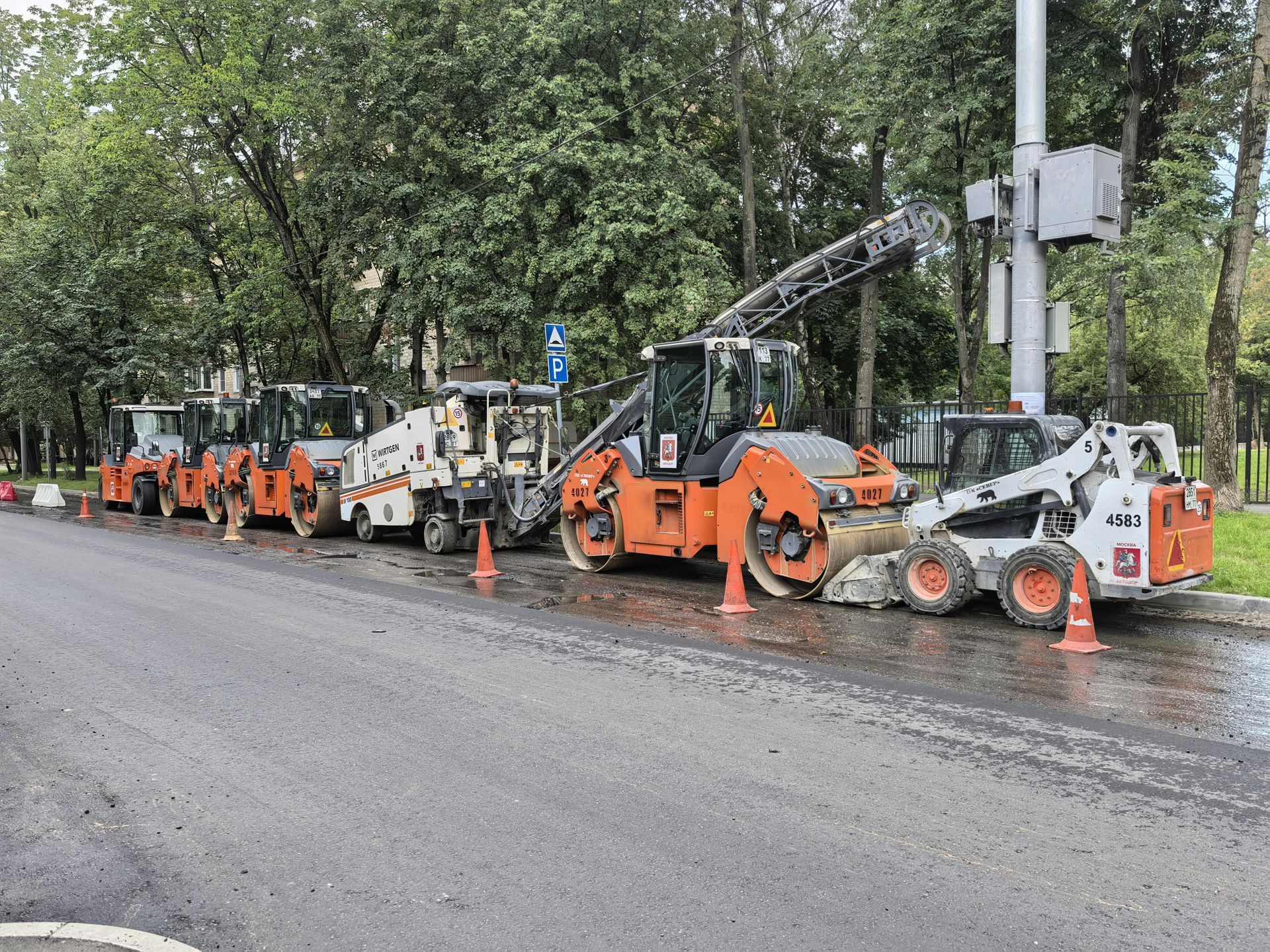 Construction vehicles, including rollers and a bobcat, parked on a freshly paved road.