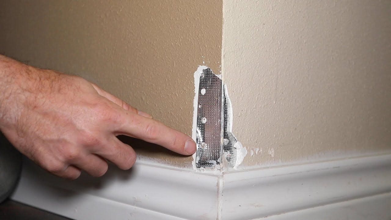 Bathroom with concrete wall, floating sink, gold faucet, and wooden shelf holding glasses.