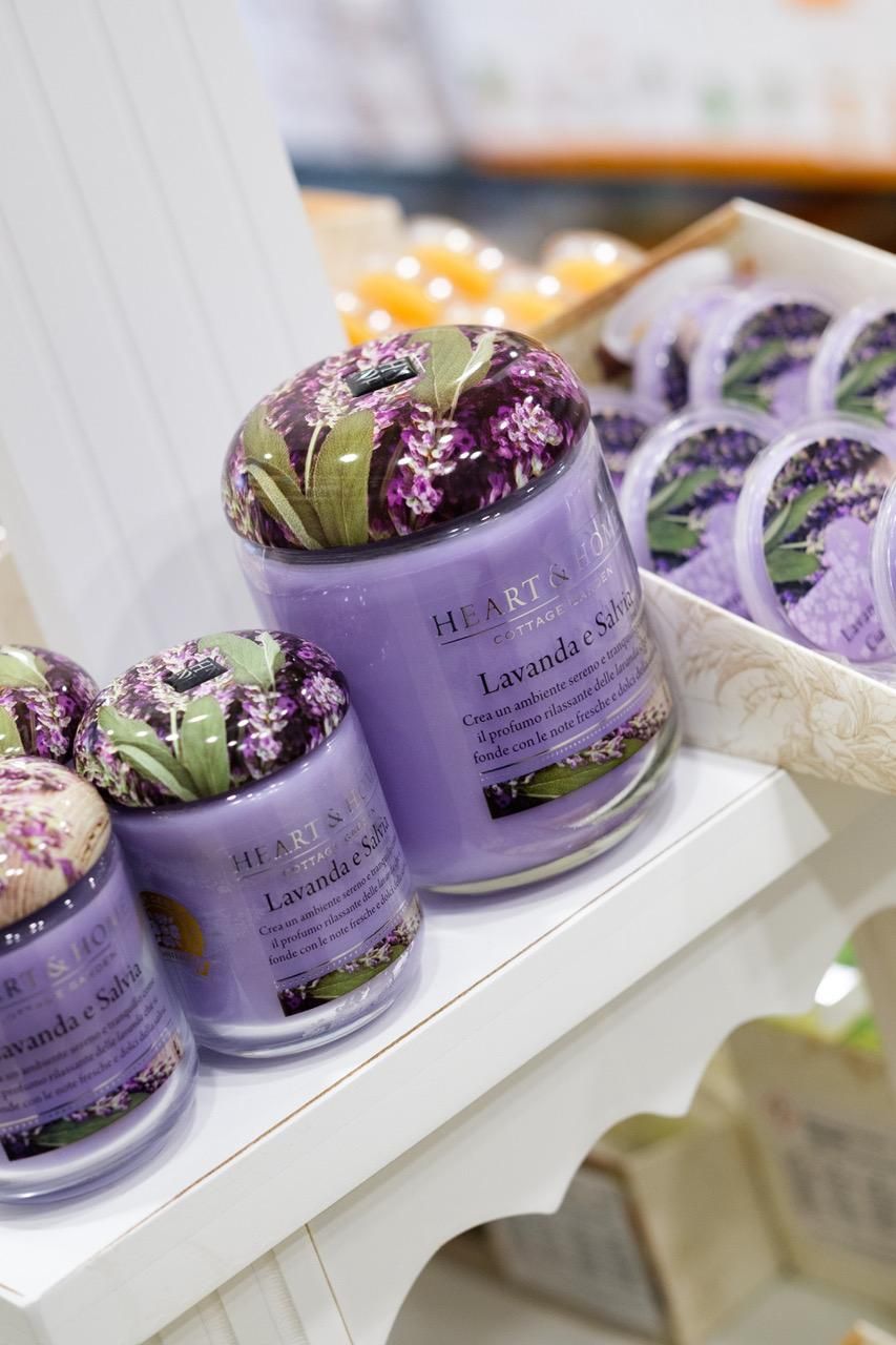Candele profumate alla lavanda su una mensola bianca. Barattoli di vetro viola con coperchi decorati a fiori.