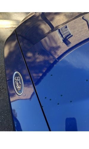 A blue ford car with rock chips using traditional automotive touch up on the hood. 