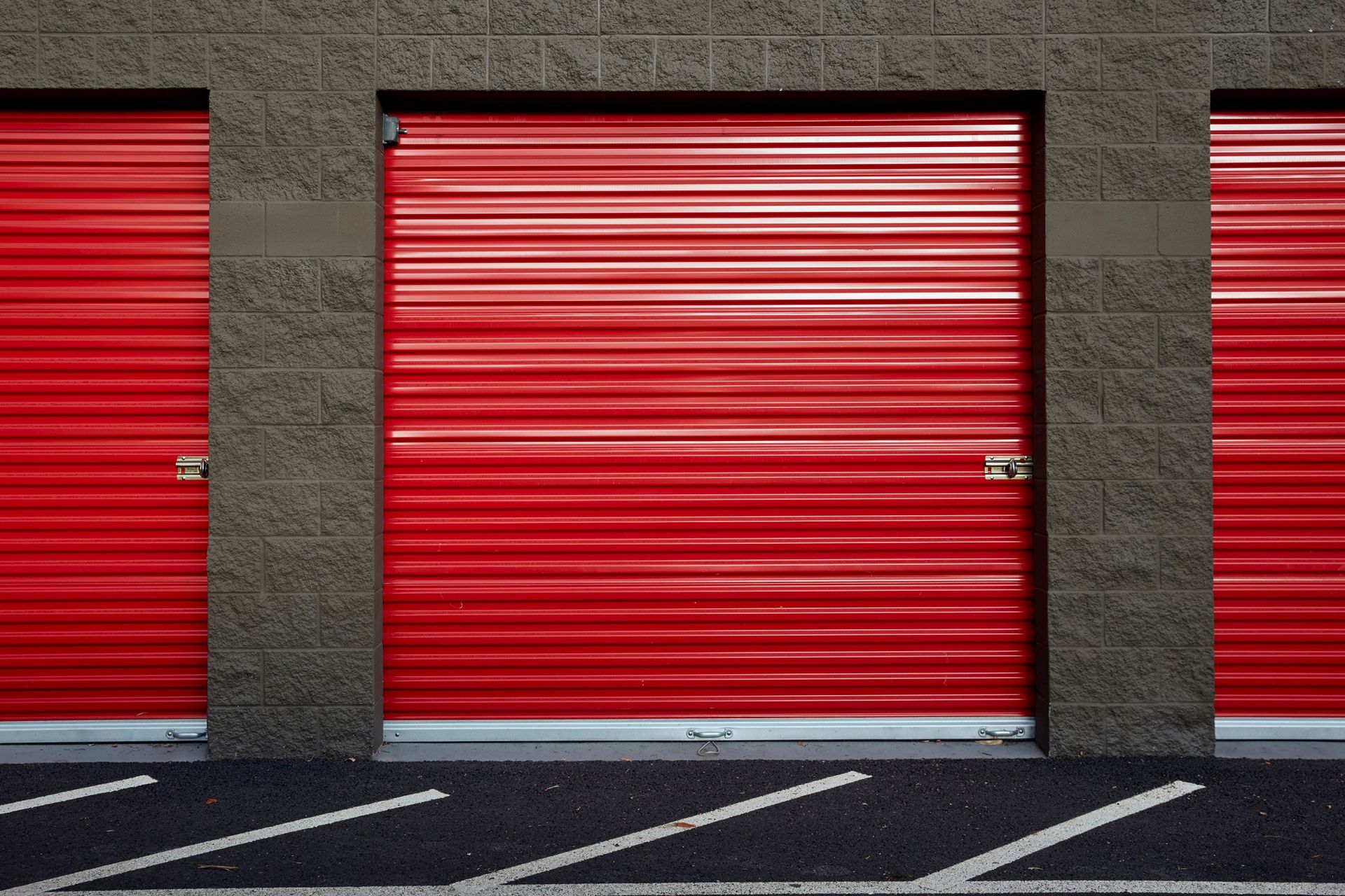 A row of red garage doors on a brick building.