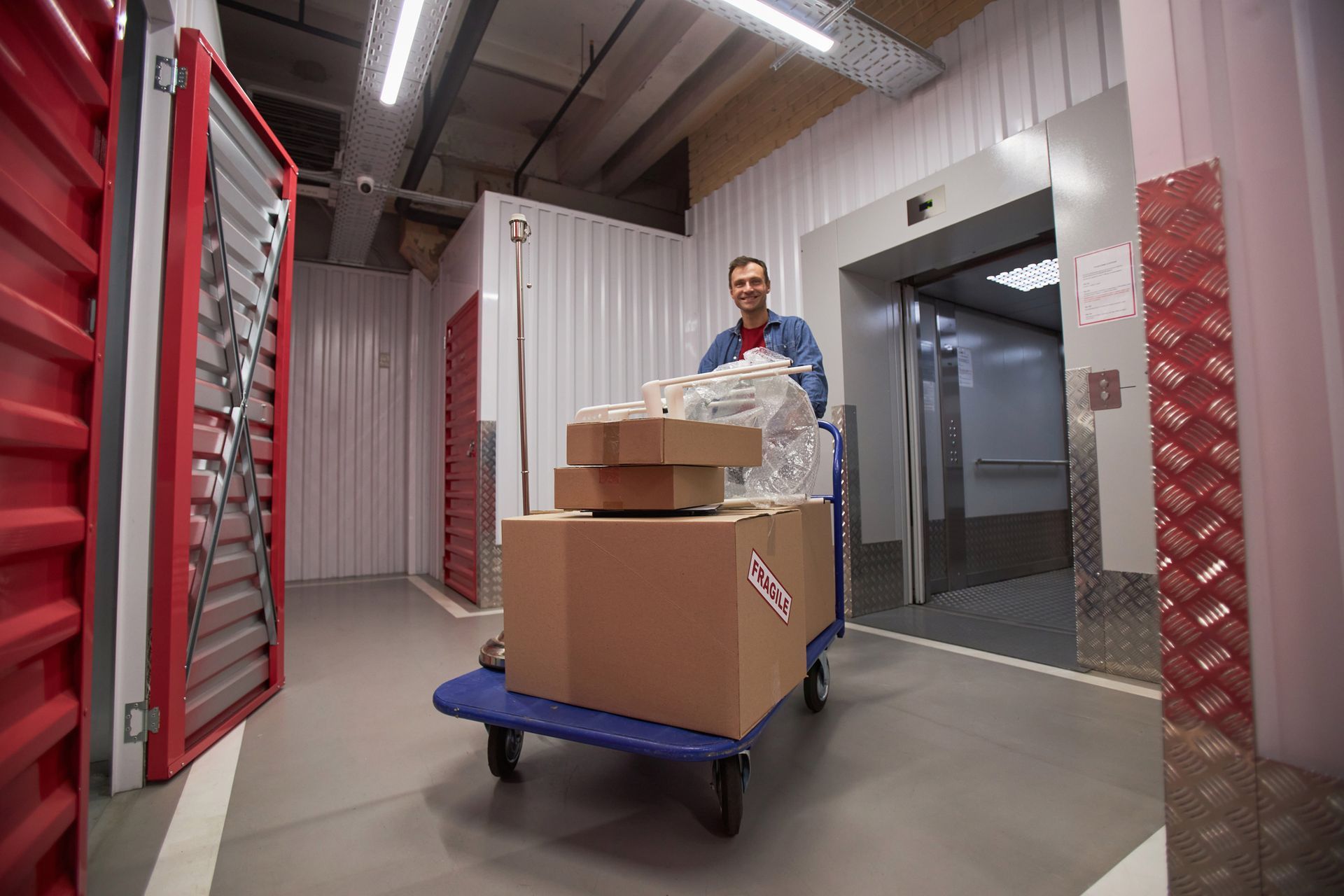 A smiling man is pushing a cart with cardboard boxes to his self-storage unit. A smiling man is pushing a cart with cardboard boxes to his self-storage unit.