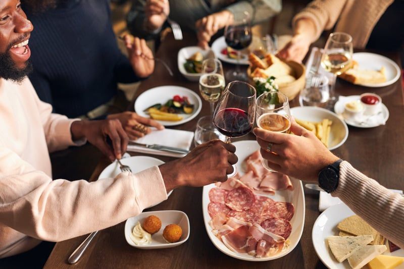 Friends sharing a meal and toasting with wine around a table of appetizers and charcuterie.