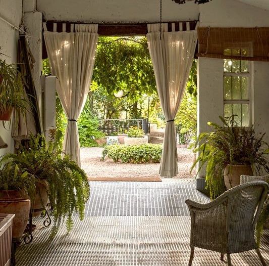Open patio with white curtains, wicker chairs, and lush garden view beyond the doorway