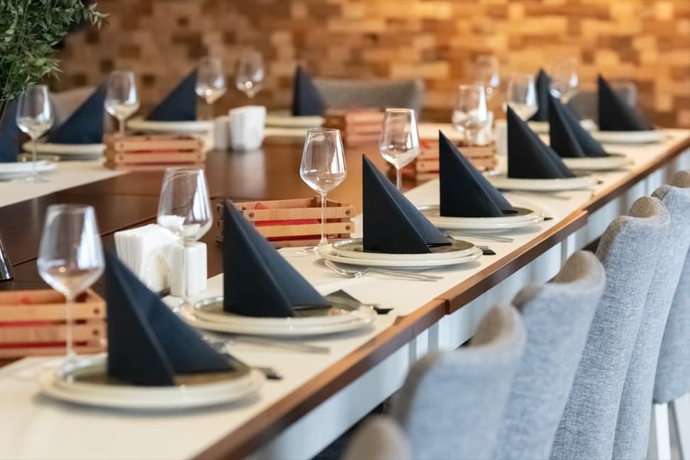 Neatly set dining table with black folded napkins, wine glasses, and plates in a warm restaurant setting