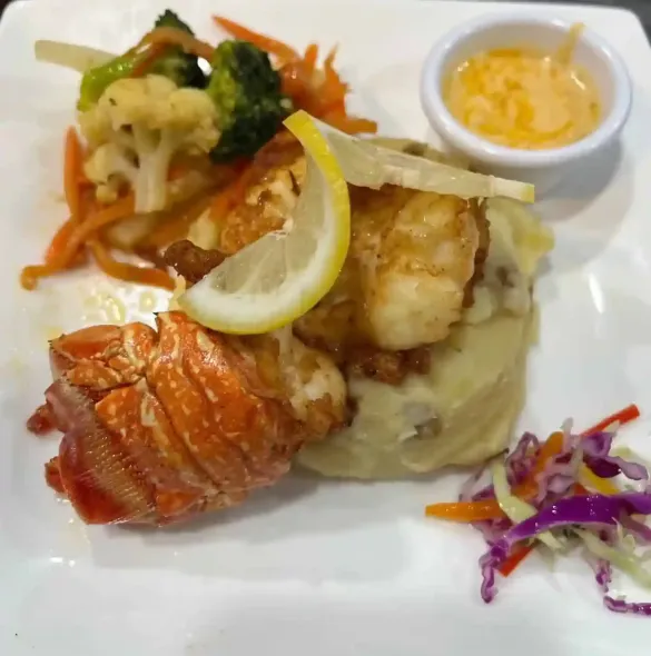 Lobster tail and seared fish with mashed potatoes, lemon garnish