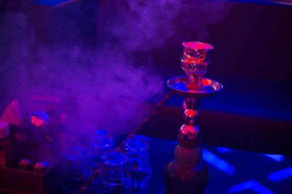 Hookah with glowing red bowl amid purple smoke in a dimly lit lounge