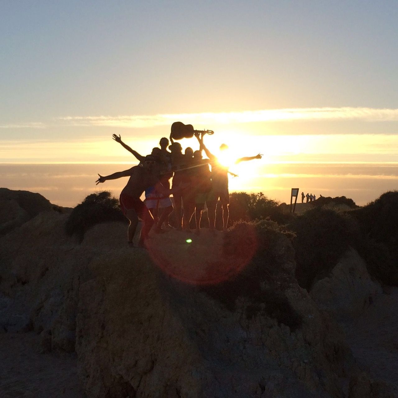 a group of people standing on top of a hill at sunset