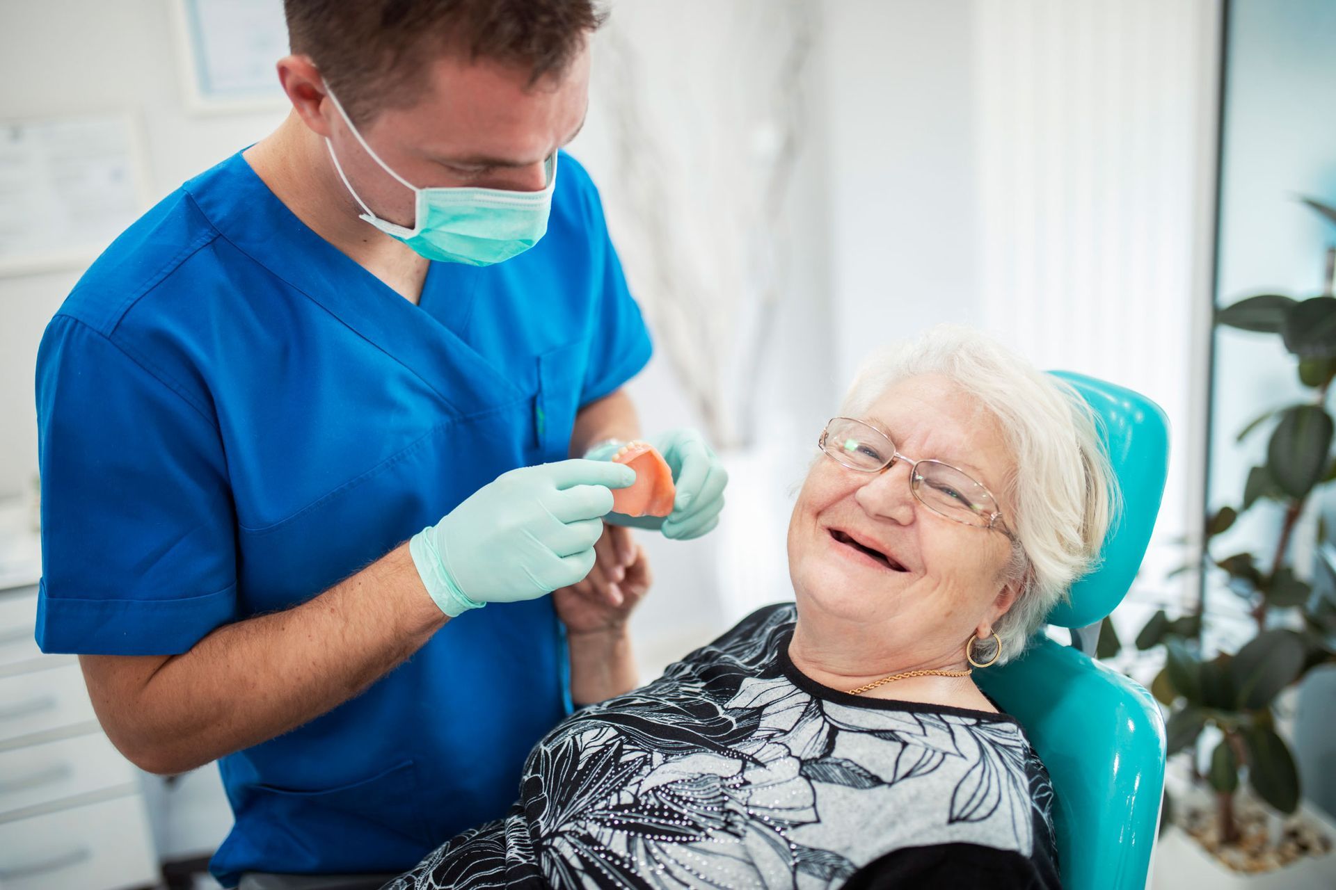 An elderly woman is sitting in a dental chair while a dentist examines her teeth.