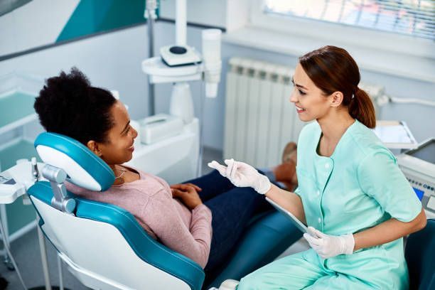 A woman is sitting in a dental chair and talking to a dentist.