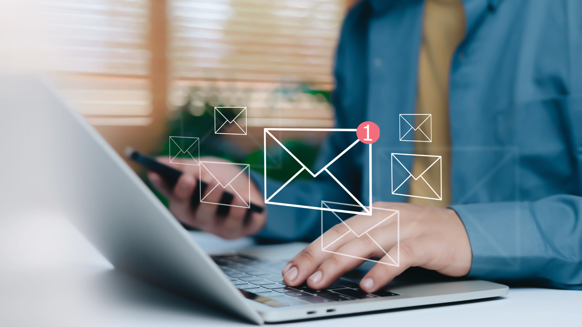 Hands typing on a laptop with floating email icons on the screen in a blurred office setting