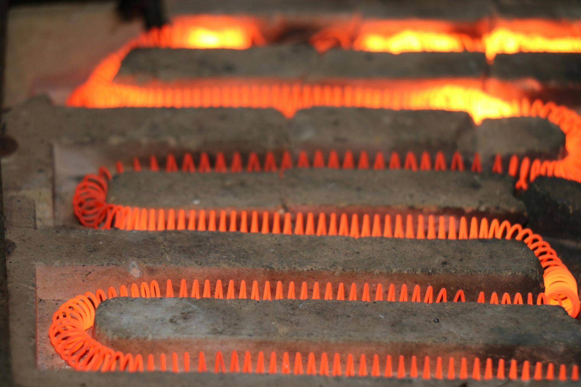 Glowing orange heating element coils threaded between rectangular, grey ceramic bricks.