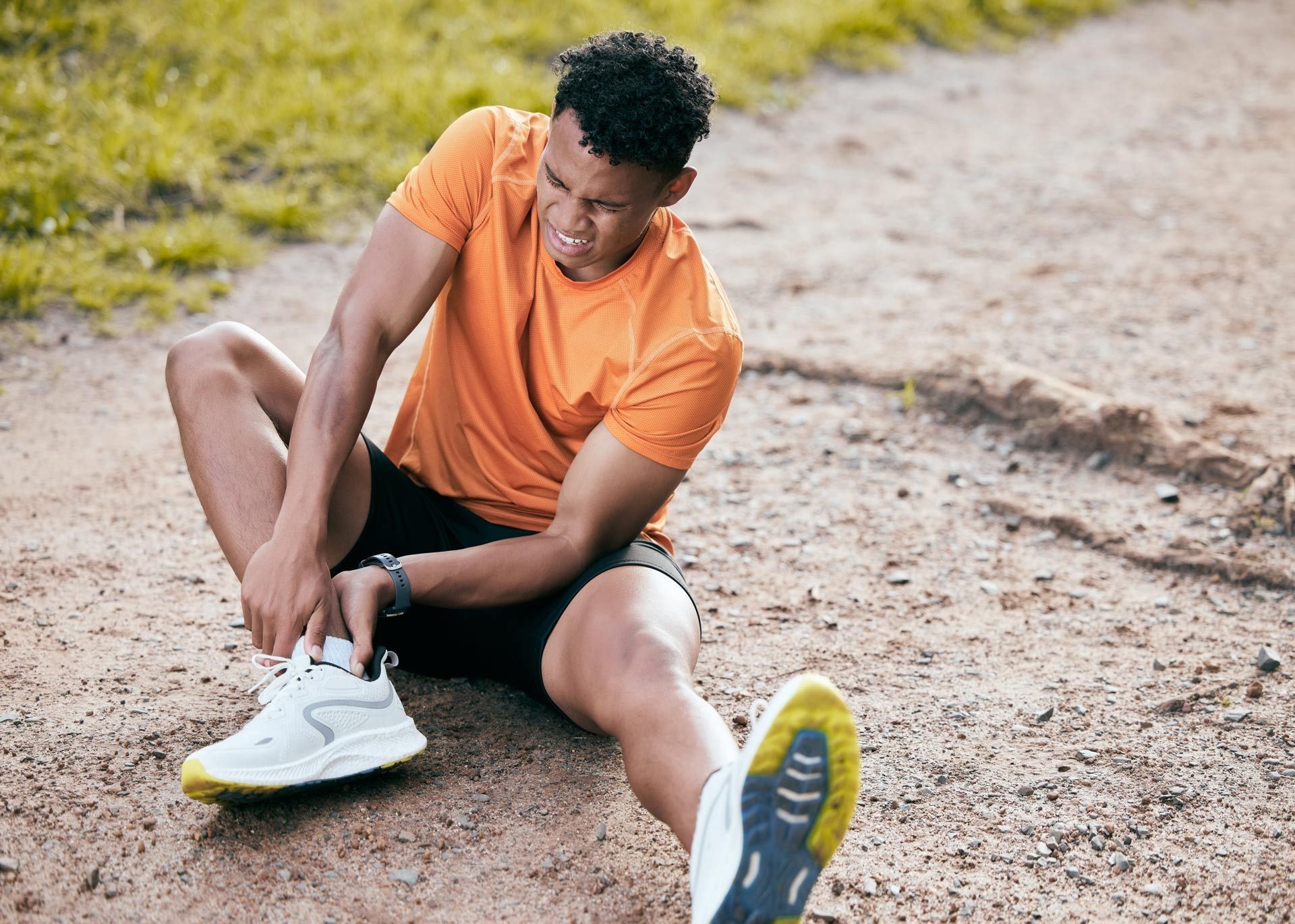 A man is sitting on the ground tying his shoes.