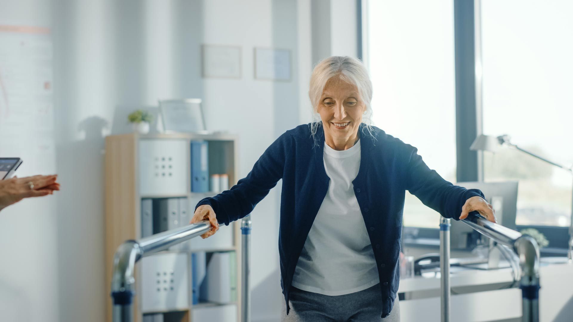 An elderly woman is using a walker to walk in an office.