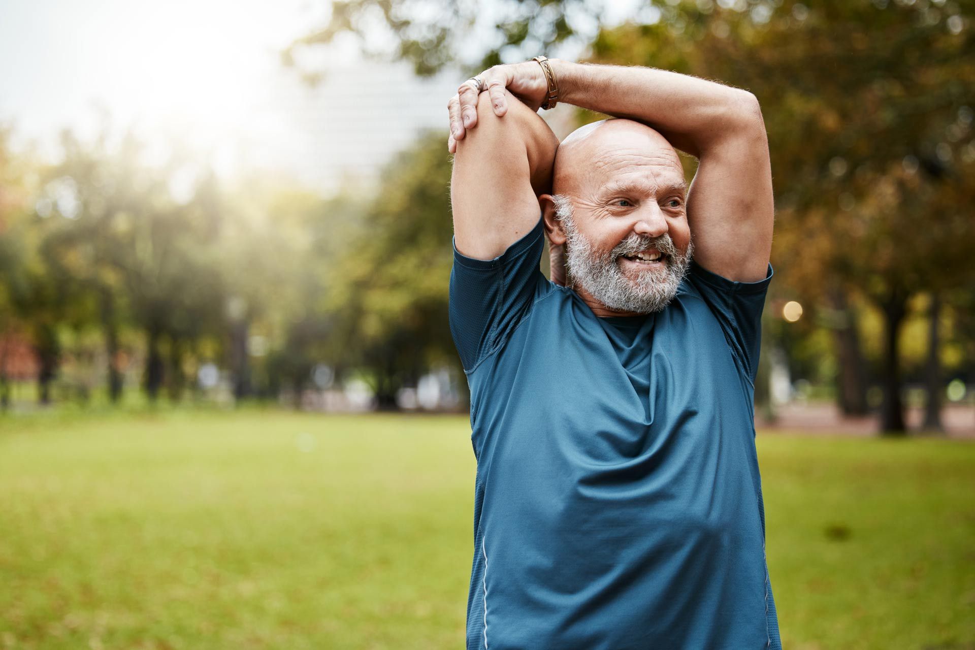 An older man is stretching his arms in a park.