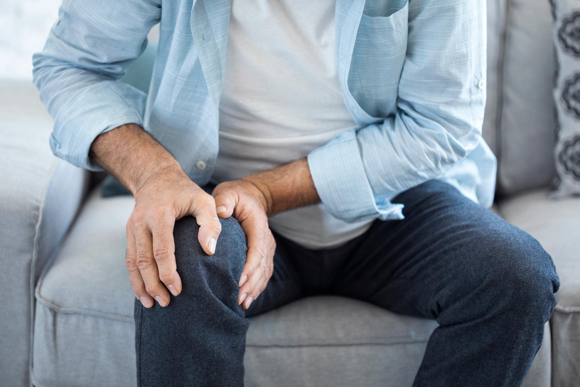 A man is sitting on a couch holding his knee in pain.