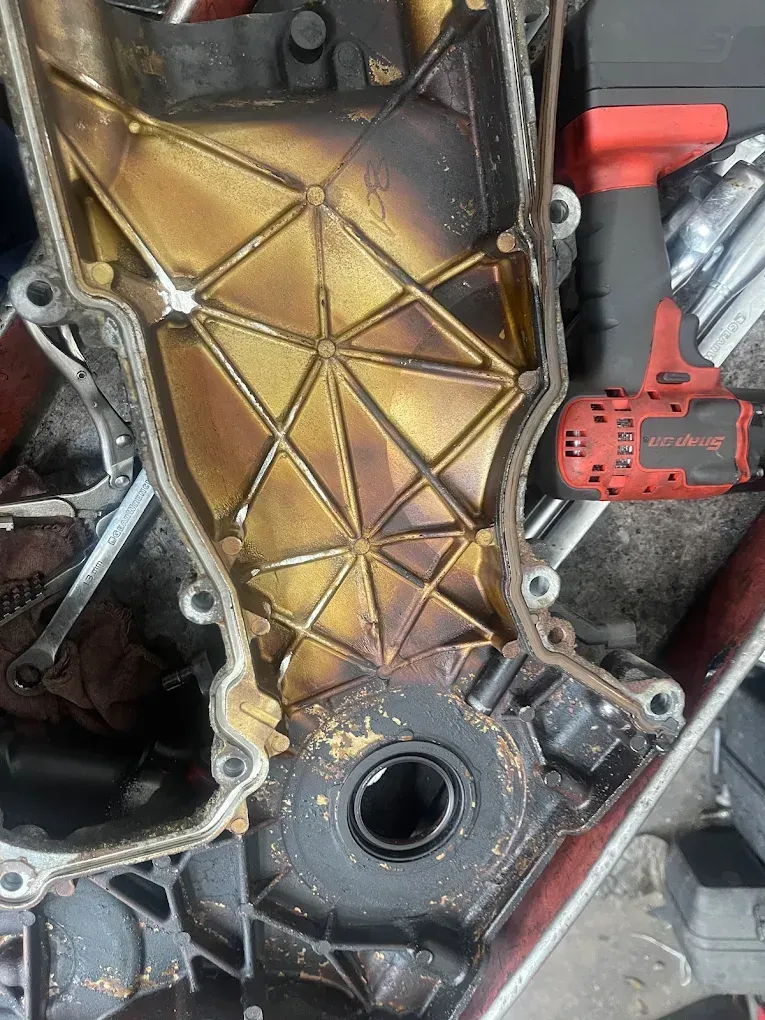 Engine timing cover, gold and black, showing oil residue and seal.