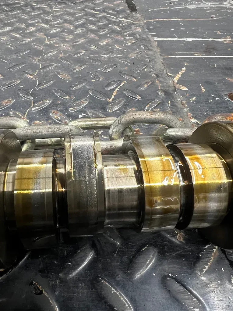 Crankshaft with oil, resting on a diamond plate surface.