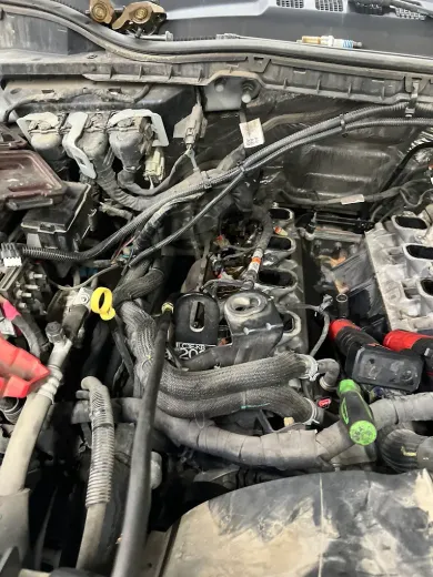 Car engine bay with removed parts; tools scattered. Dirty, black engine with various hoses and wires.
