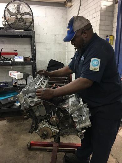 Mechanic in blue uniform and cap working on a car engine in a garage.