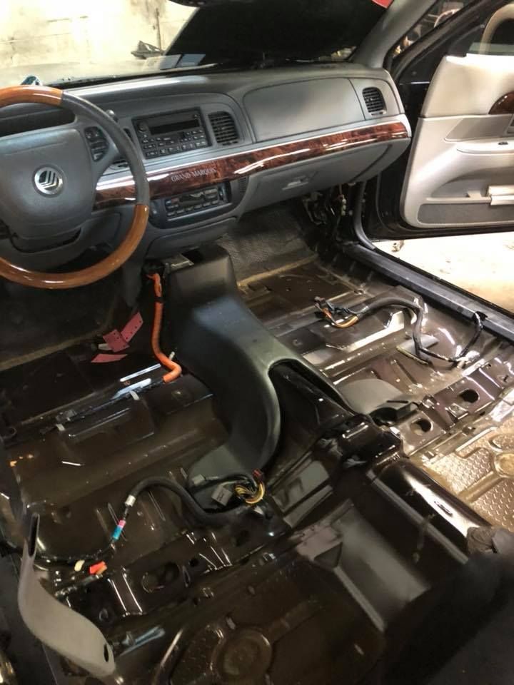 Interior of a car with the seats and carpet removed. Black flooring is visible, with wiring exposed.