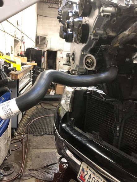 Engine partially assembled, with a large black hose extending toward a radiator, in a garage setting.