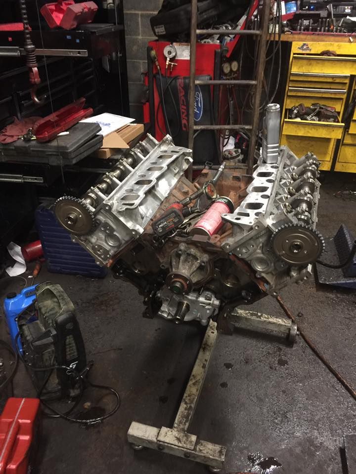 Car engine on a stand in a garage. Exposed components, oil and tools visible.