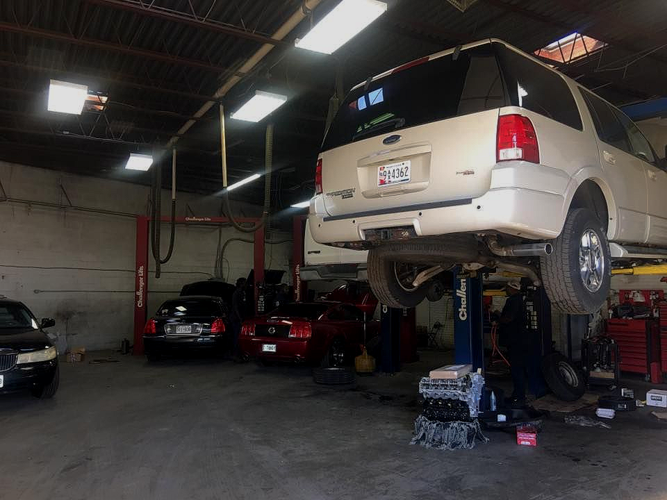 Ford Expedition raised on a lift inside an auto repair shop. Other cars, tools, and fluorescent lights are visible.