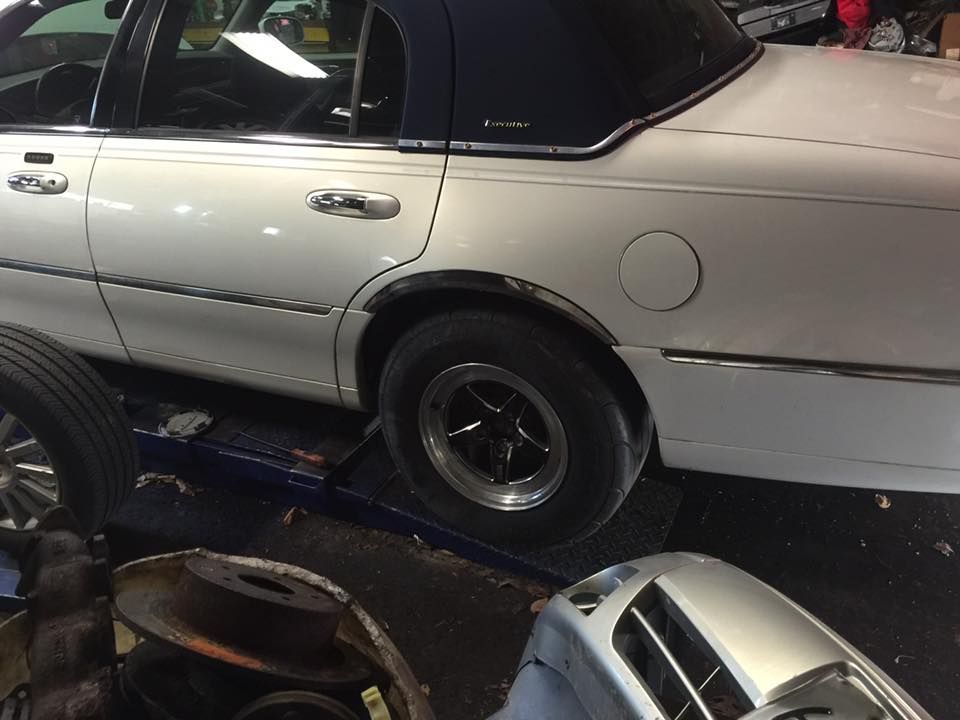 White Lincoln sedan on a lift in a garage, with a blue roof and black wheels.