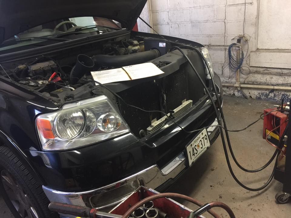 Black Ford pickup truck with the hood open in a garage being serviced.