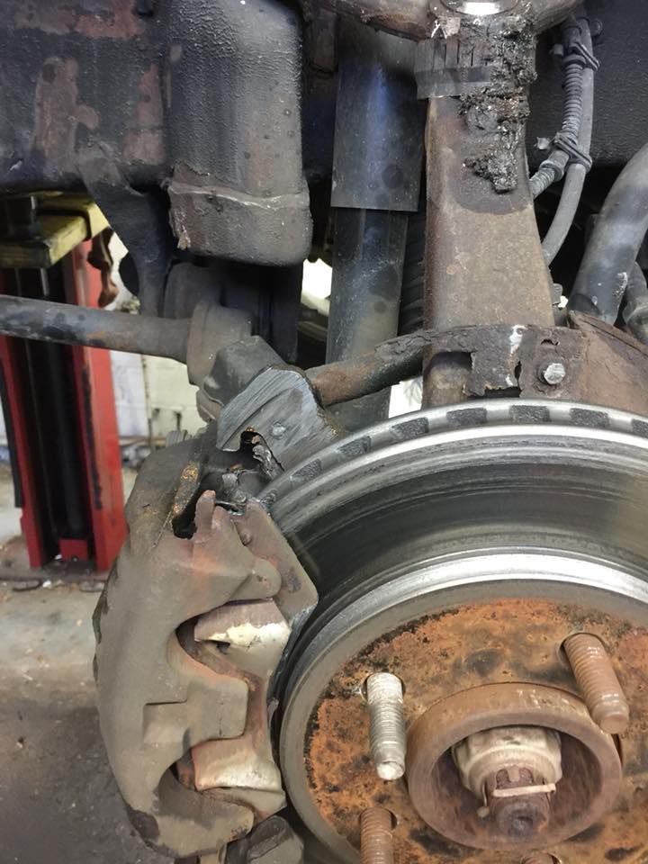 Close-up of a rusty car suspension, including brake rotor, caliper, and shock absorber.