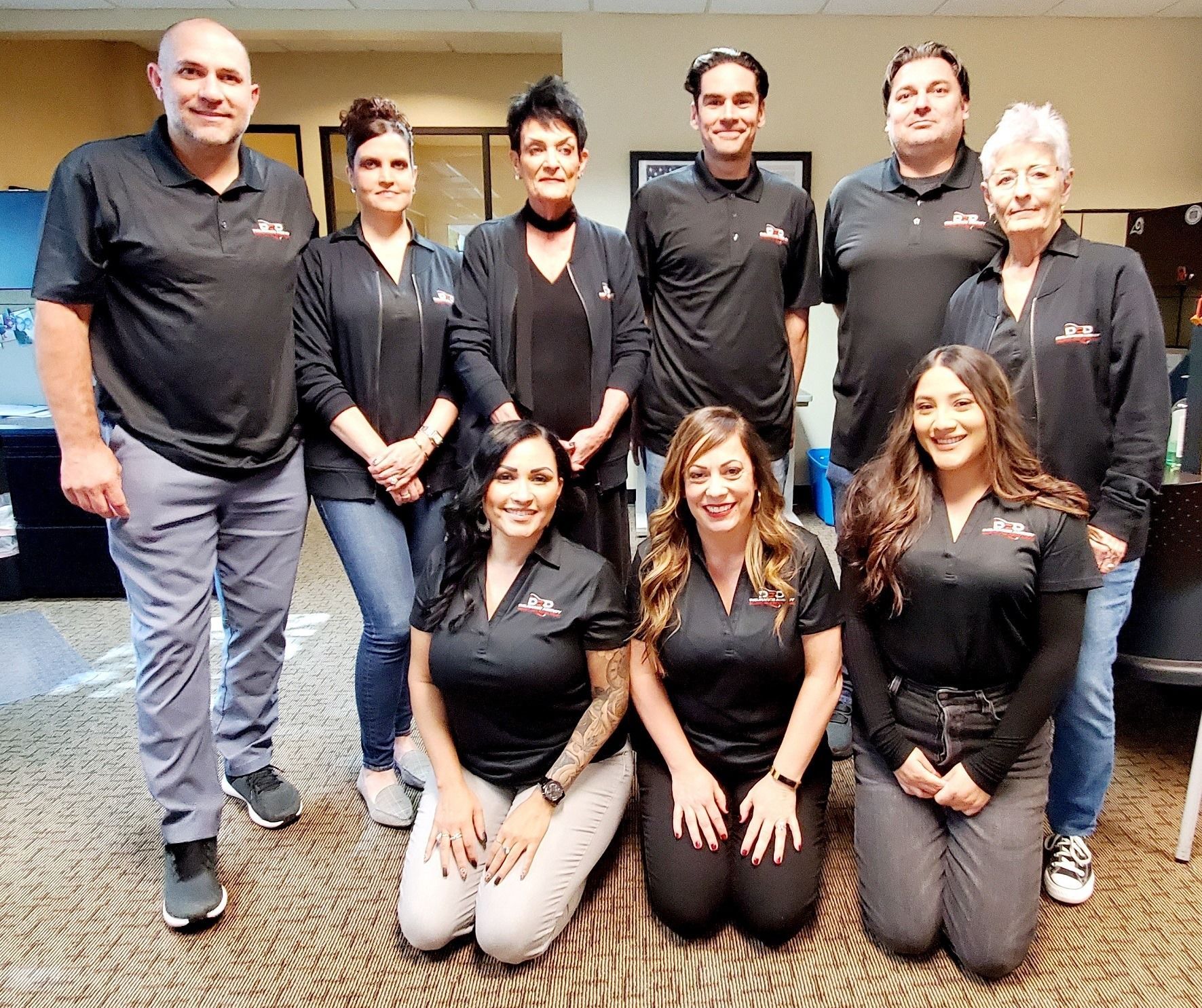 The DRD Team of people in black shirts, some kneeling, posing indoors.