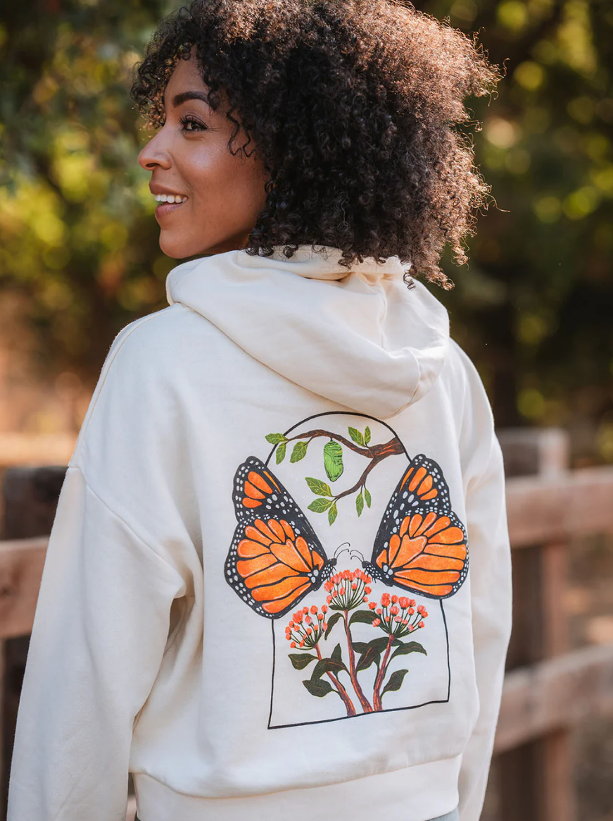 A woman is wearing a white hoodie with two butterflies on the back.