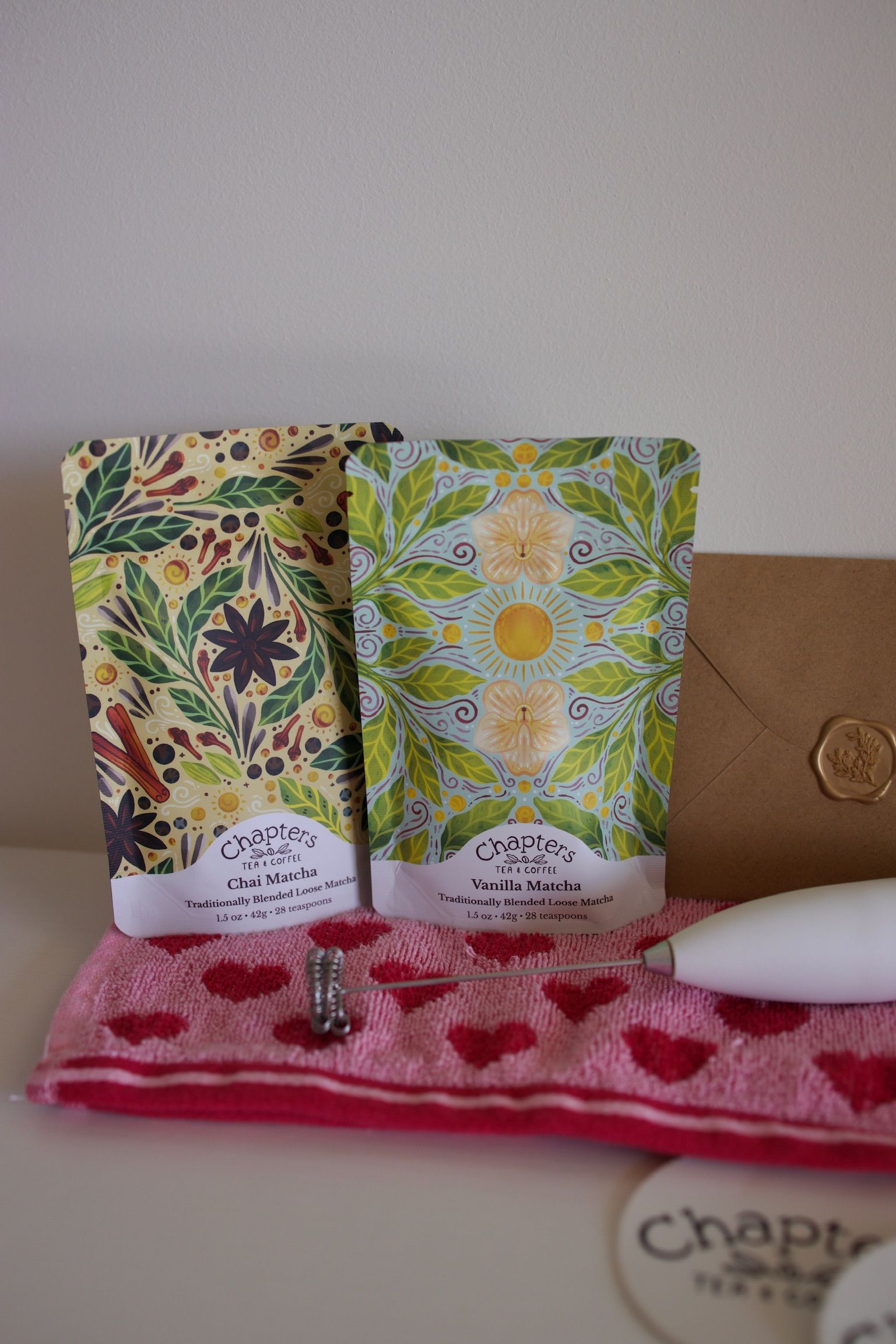 Two bags of soap are sitting on a pink towel next to an envelope.