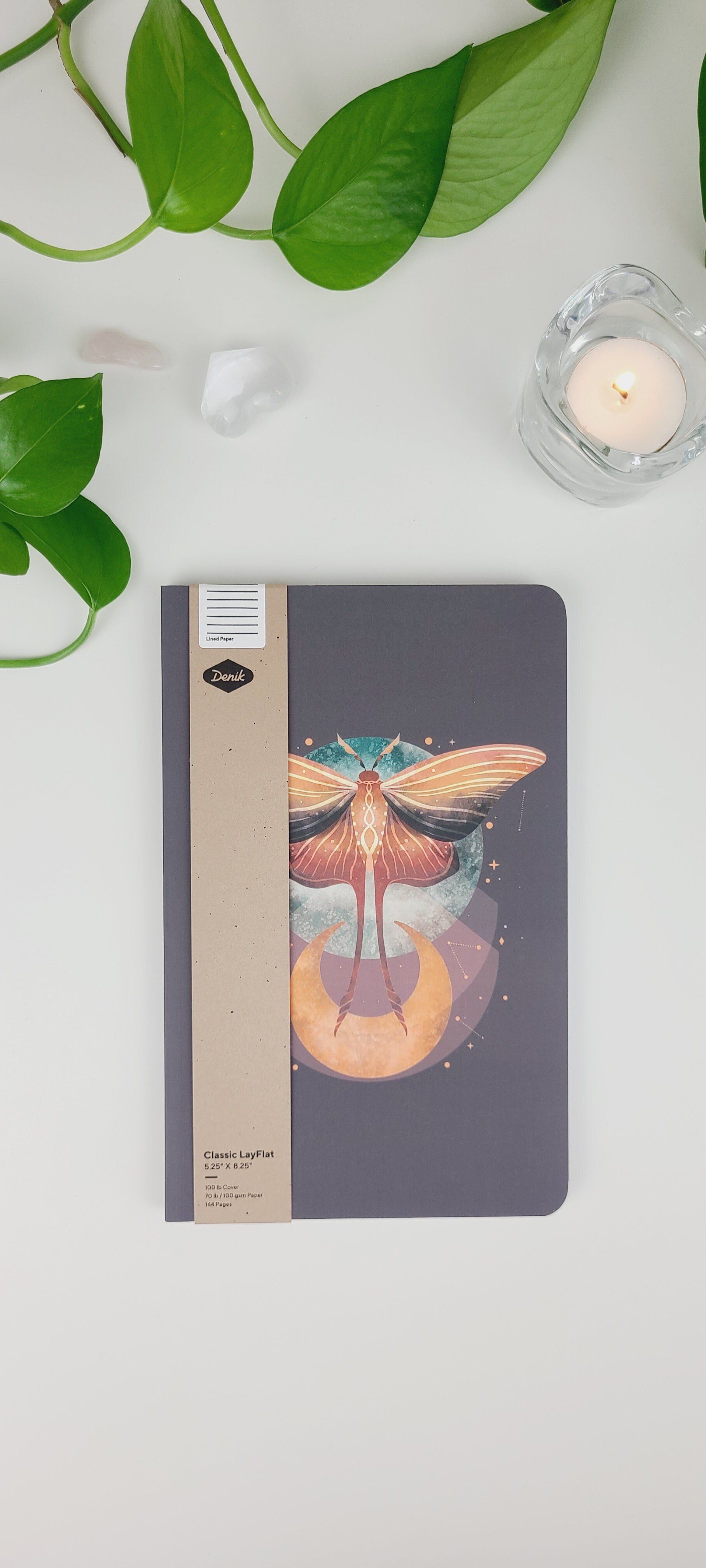a notebook with a dragonfly on the cover is sitting on a table next to a plant and a candle .