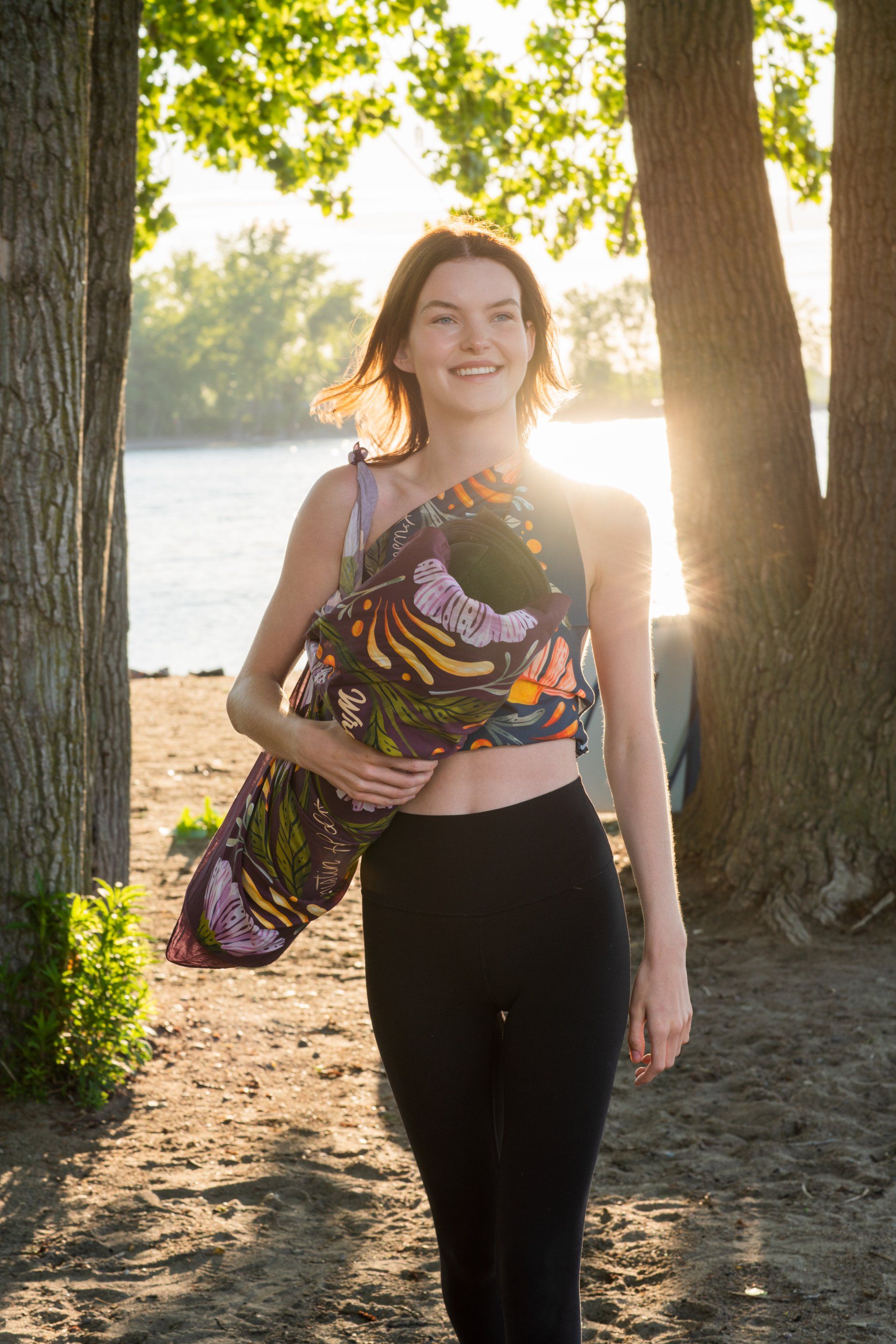 a woman is walking on the beach holding a yoga mat .