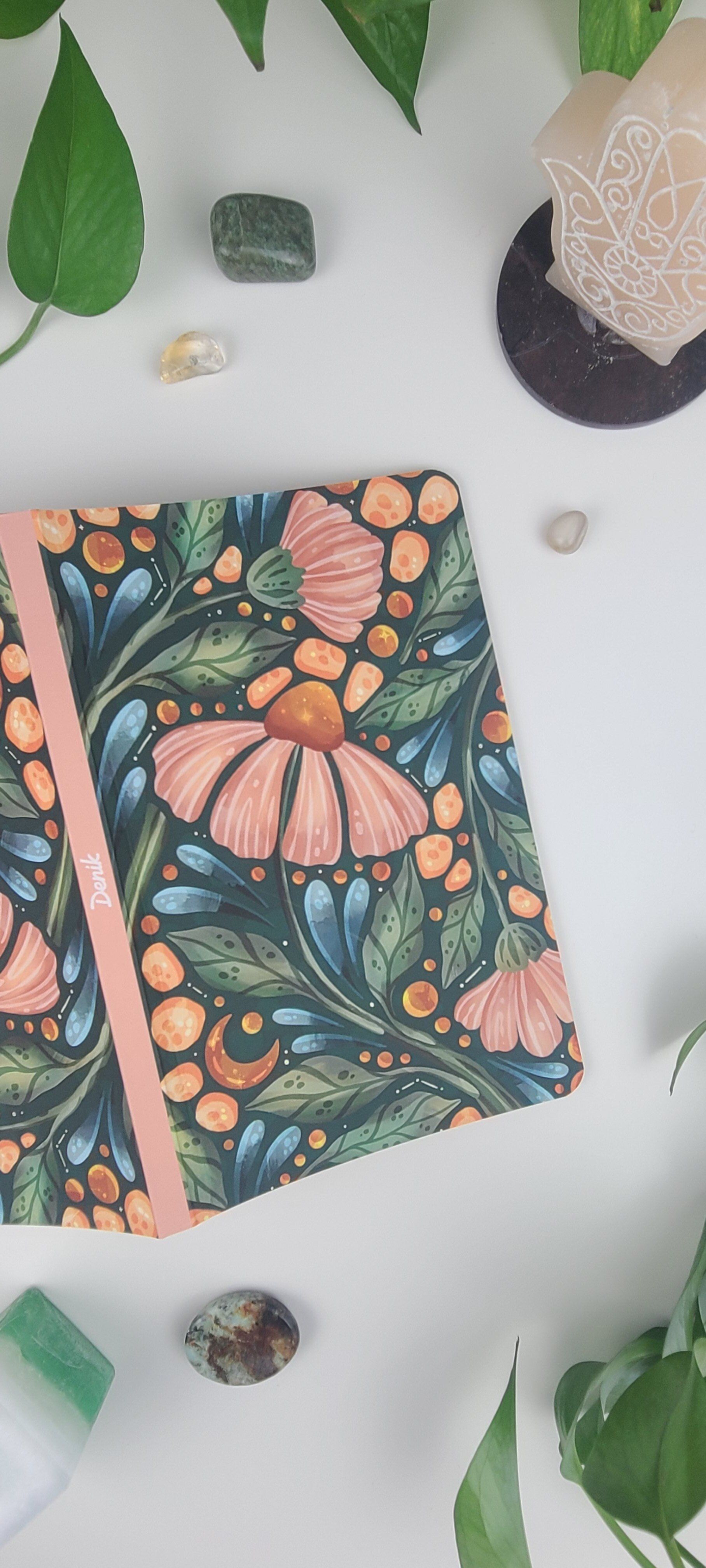 a notebook with a floral design is sitting on a table surrounded by plants and crystals .
