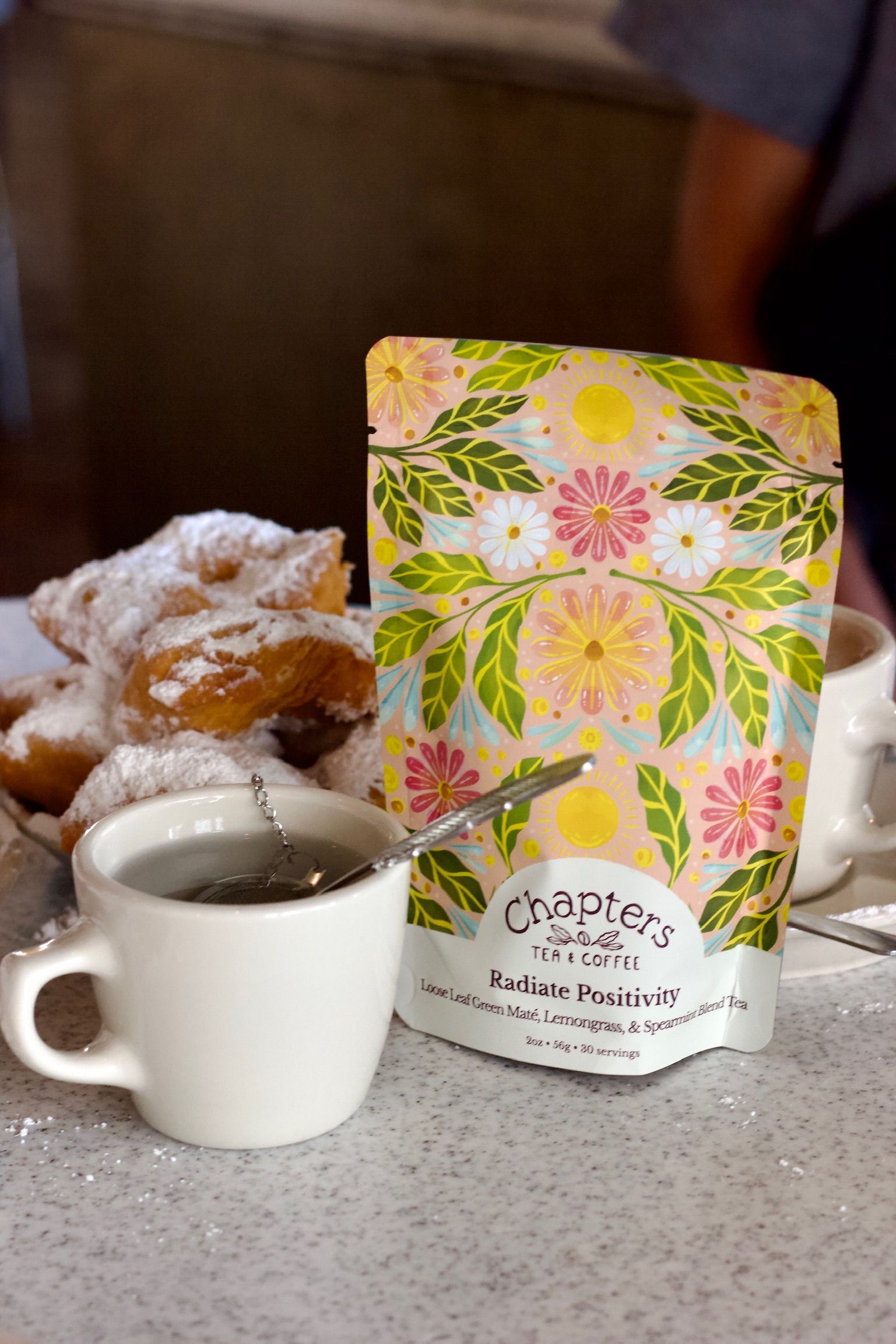 A bag of chapter 's tea is sitting on a table next to a cup of tea and donuts.