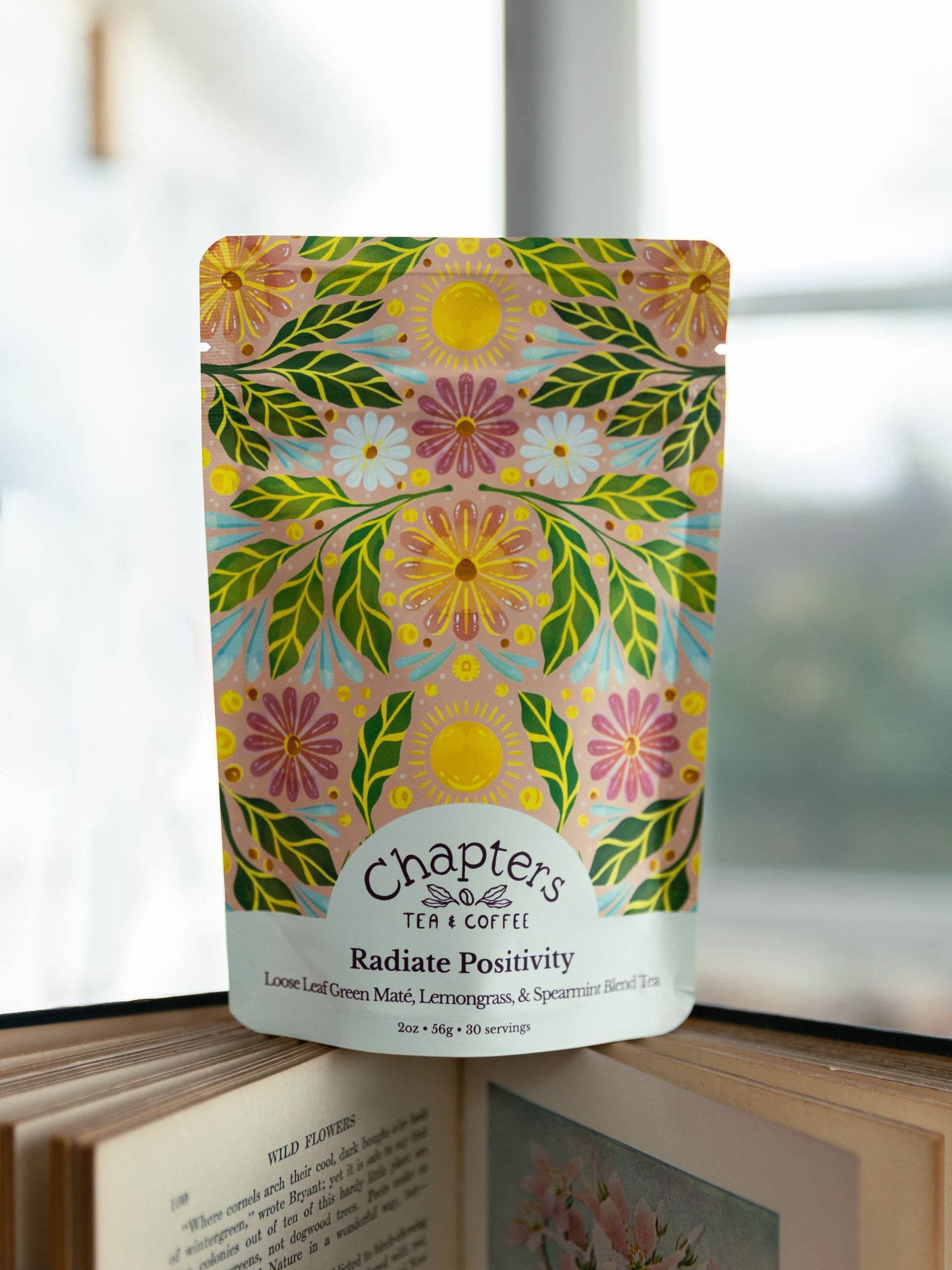 A bag of tea is sitting on top of a book next to a window.