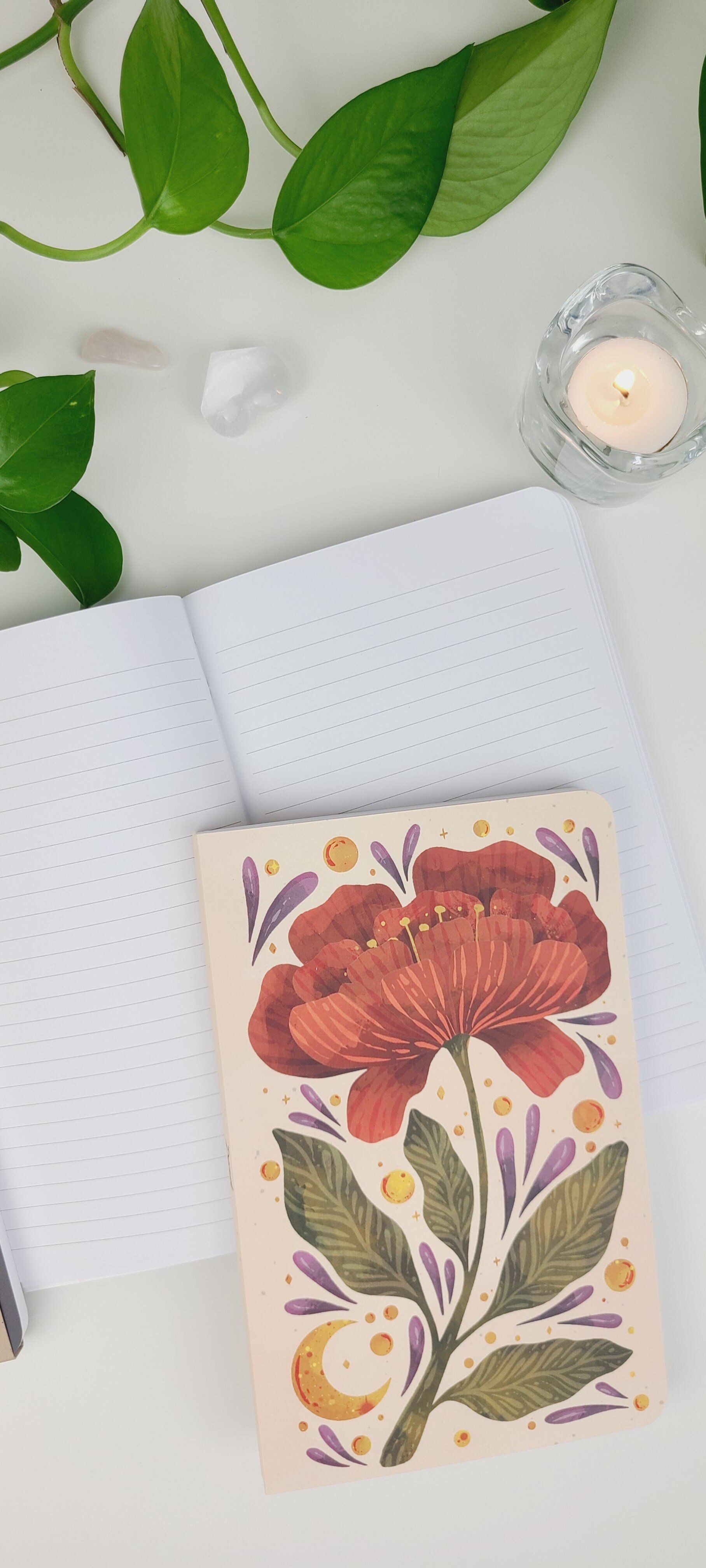 a notebook with a flower on it is sitting on a table next to a candle .