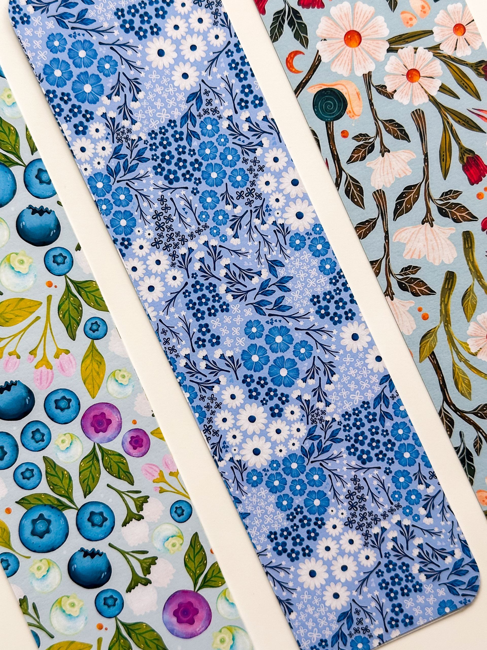 Four bookmarks with flowers and dragonflies on them are sitting on a table.