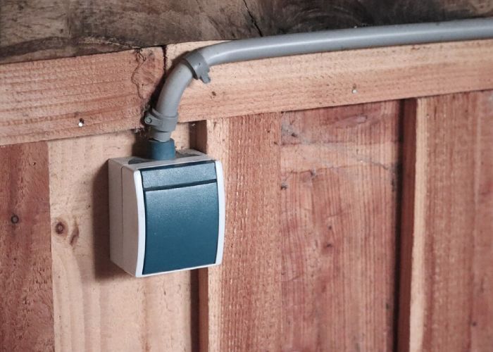 A wall-mounted electrical switch with surface conduit wiring is installed on a wooden panel for power control.