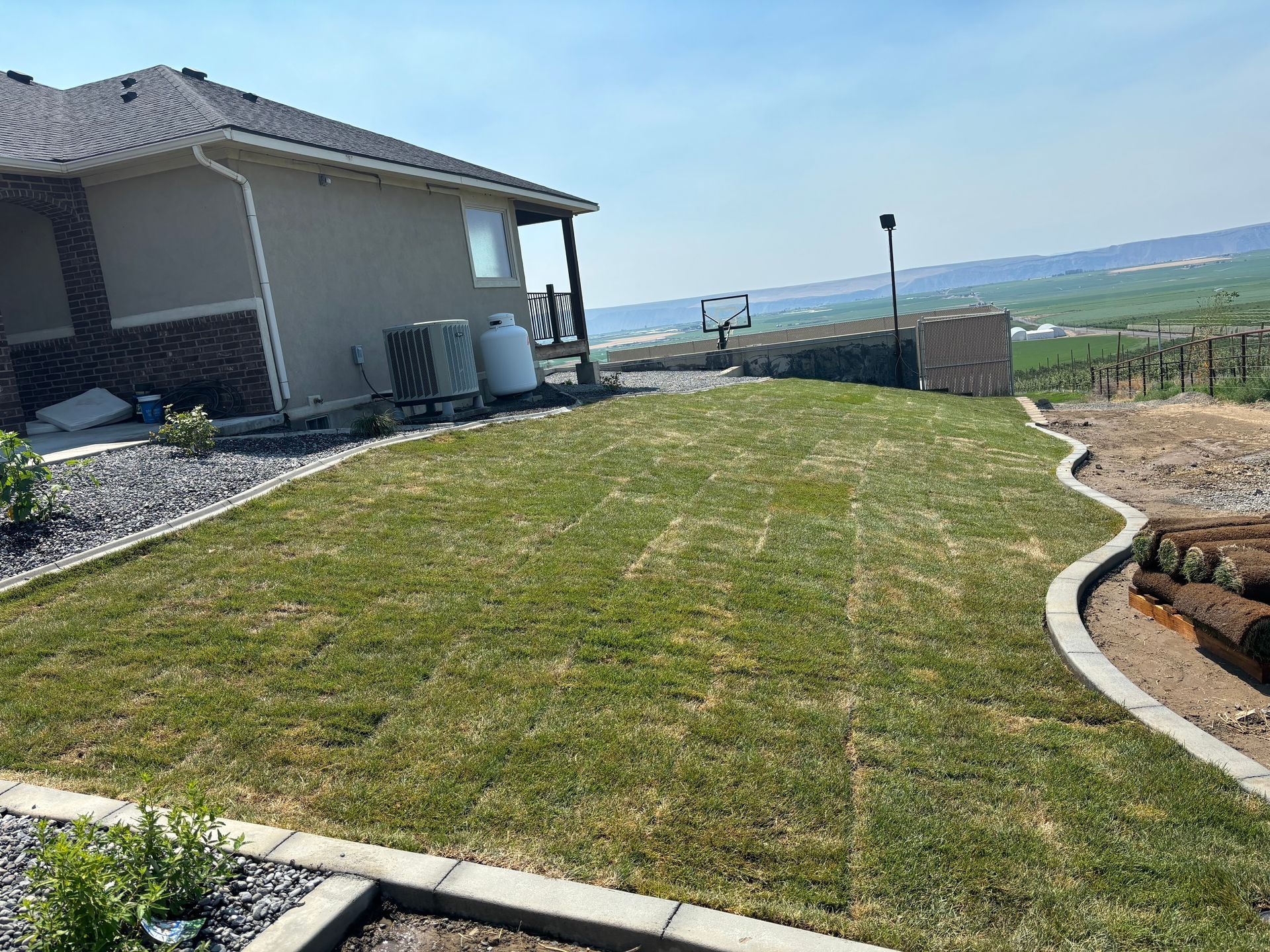 A freshly laid sod lawn bordered by concrete blocks next to a tan house under a bright blue sky.