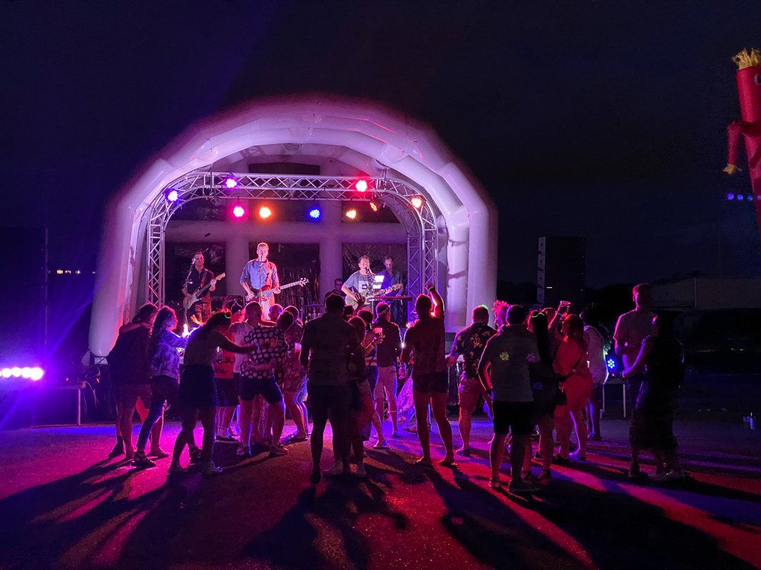 Inflatable roof stage set up for an outdoor event at nighttime with lighting and a band and an audience