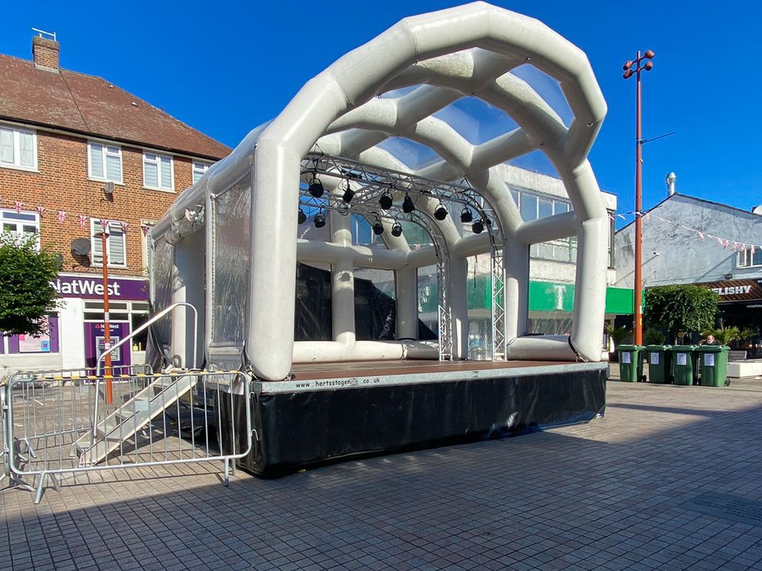 An inflatable stage set up on a concrete courtyard in a town centre with a bright blue sky above it.