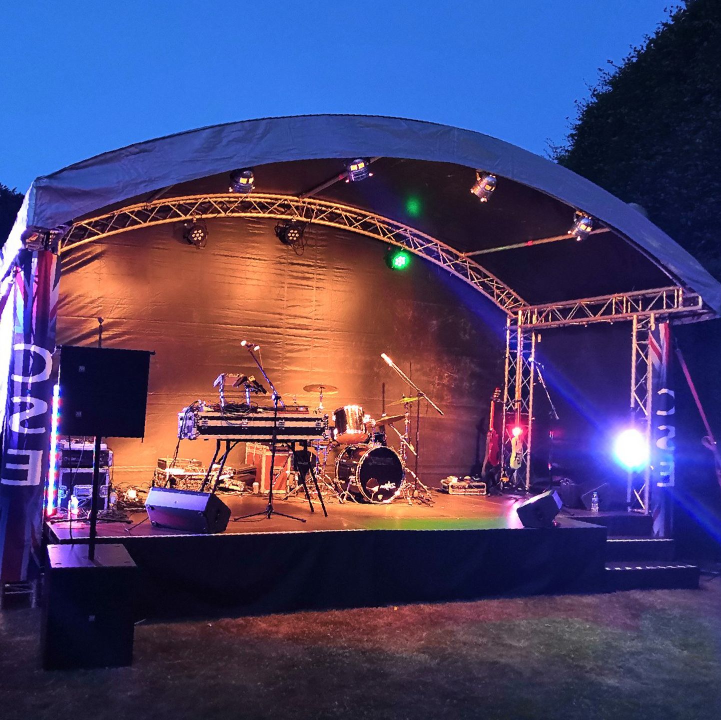 Arc truss stage set up for an event with backline and lighting