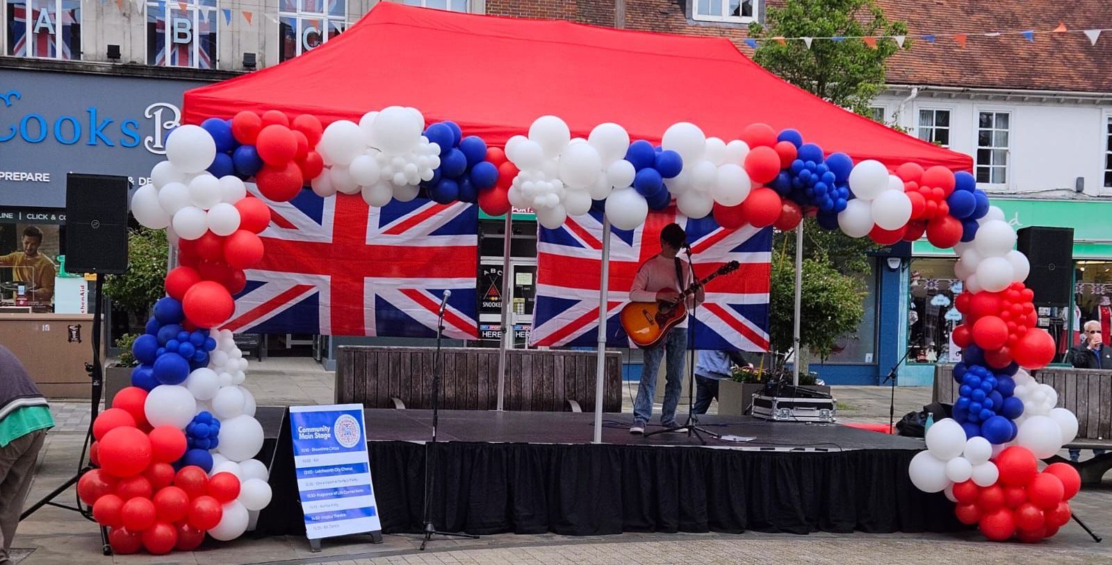 A 6metre by 3 metre modular stage with a red canopy and red, white and blue balloons around it.