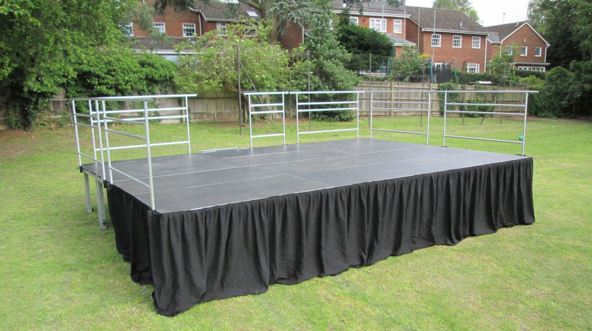 a 6 metre by 4 metre modular stage with black skirt and metal railings set up in a field