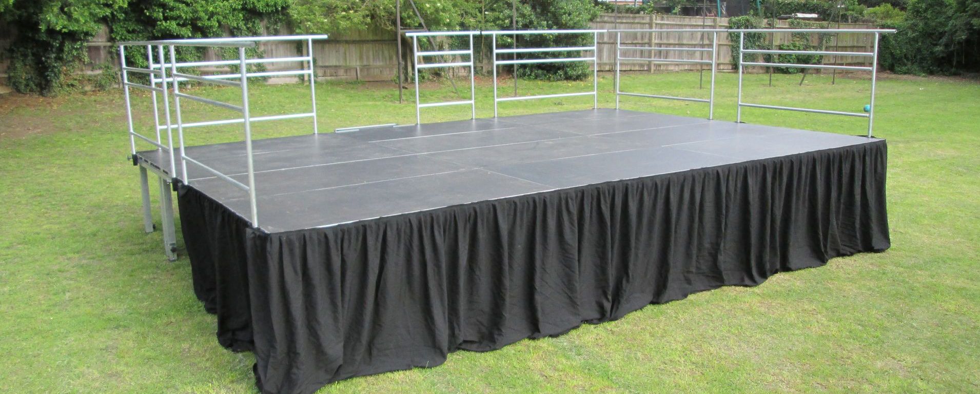 A modular stage in a field with railings and a black skirt